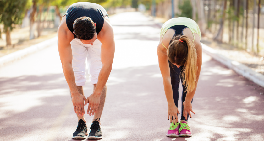 A man and woman demonstrate a gentle, straight leg toe touch stretch.